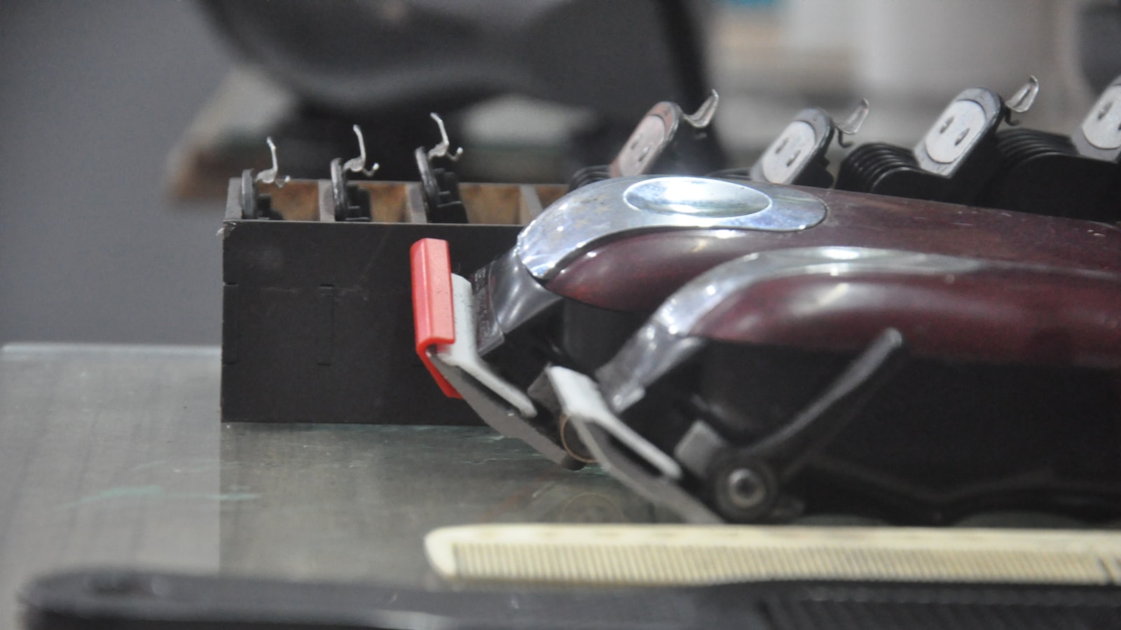 Two hair clippers and a comb on a counter with a rack of attachments behind them