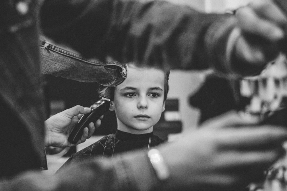 Black-and-white close-up of a young boy receiving a haircut from a barber using clippers