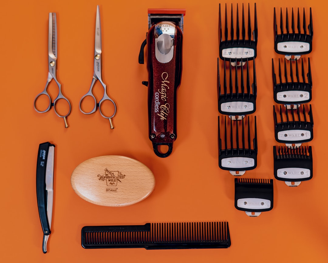 Flat lay of barber tools on an orange background: a cordless clipper, guard combs, two pairs of shears, a straight razor, a comb and a brush