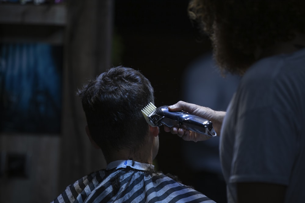 A barber uses clippers to cut the hair of a client wearing a striped cape