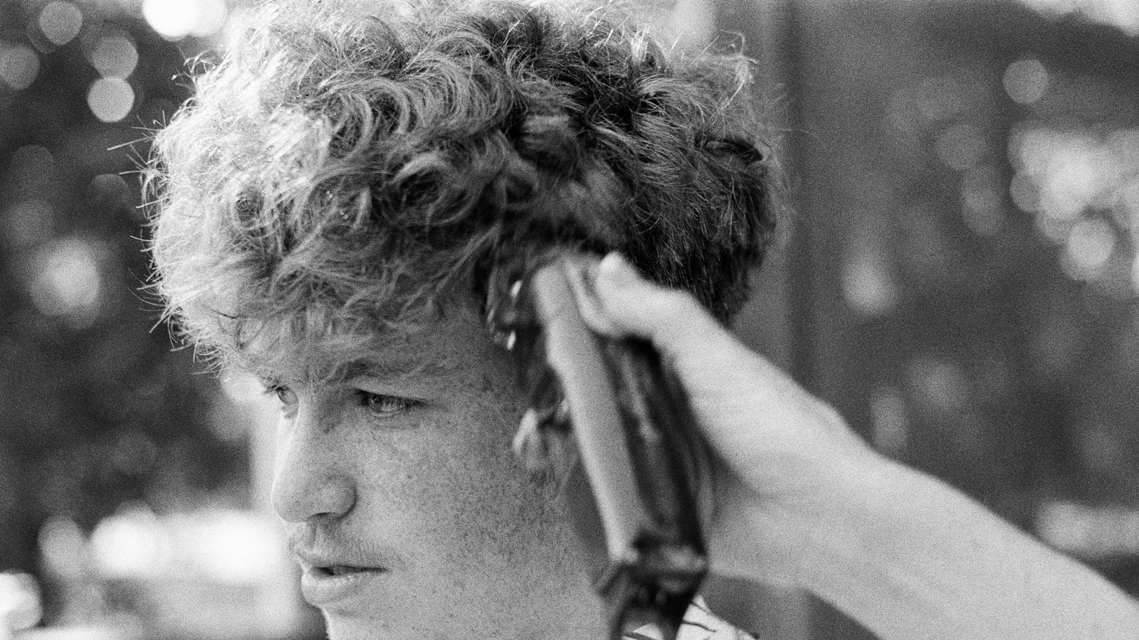 Black-and-white close-up of a person with curly hair getting a haircut with clippers