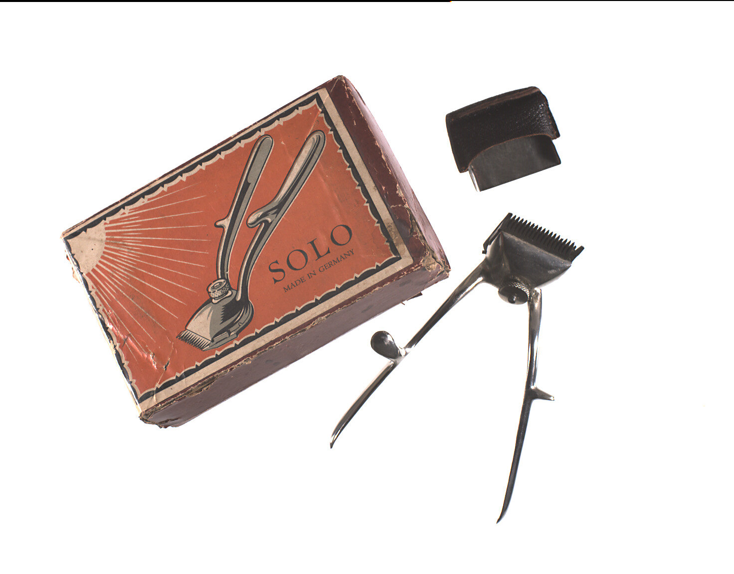 An angled box, a small metal clipper tool, and a blade cover are on white