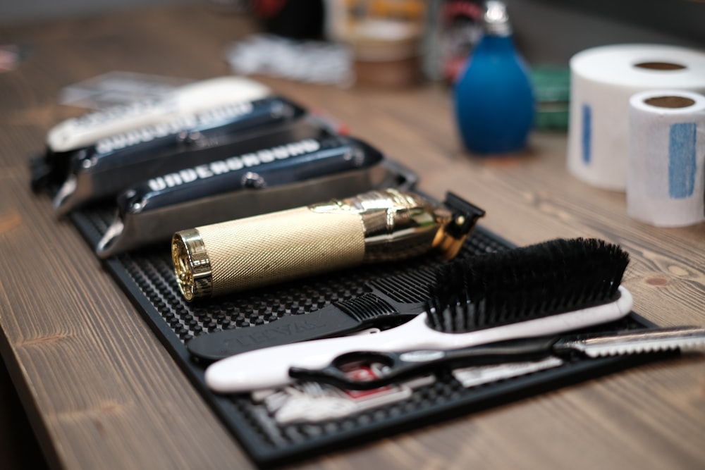 Barber tools including clippers, a brush, scissors, and a razor on a mat