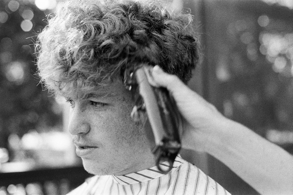 Black and white photo of a person getting their curly hair shaved with clippers