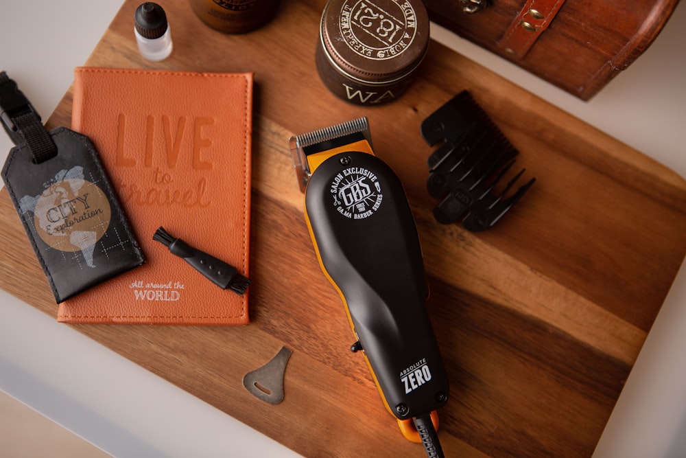 An orange hair clipper rests on a wooden board alongside a notebook, brush, and small containers