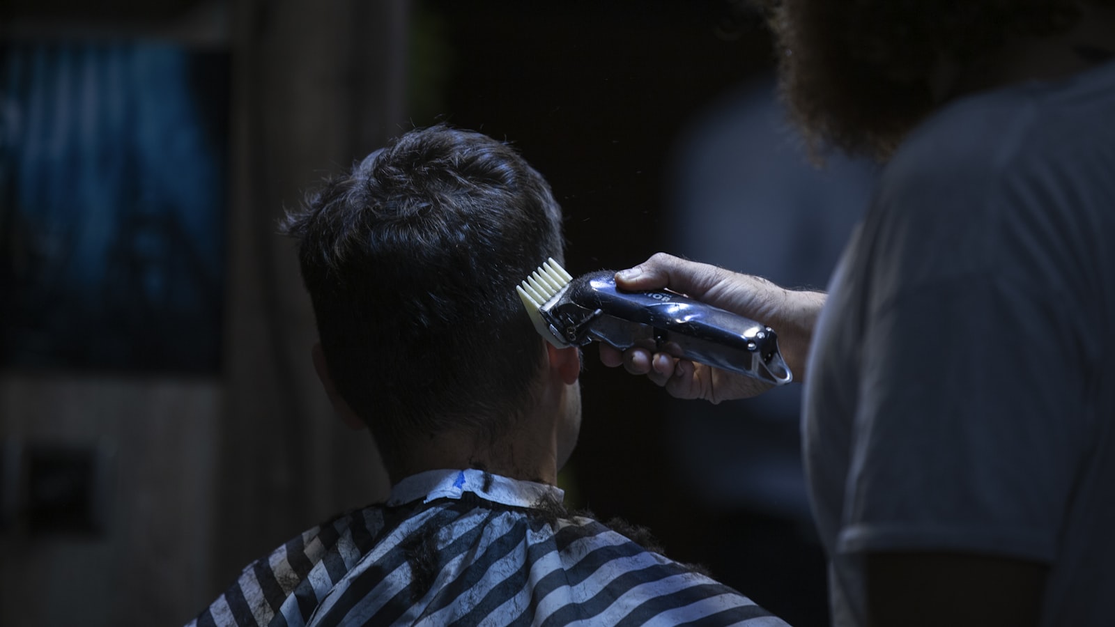 A person uses hair clippers on the back of another person's head